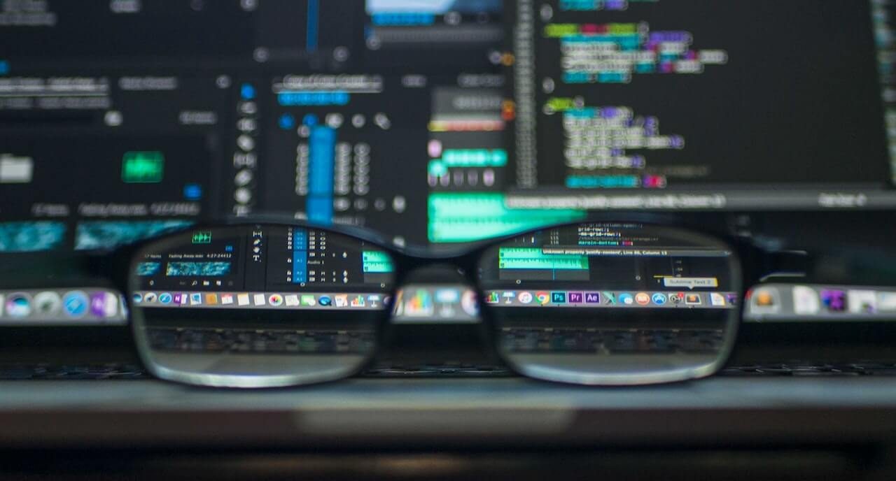 Glasses placed in front of a computer screen showing code, creating a shallow depth of field effect.